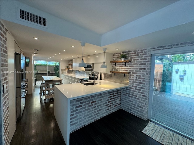 kitchen with decorative light fixtures, sink, dark wood-type flooring, and kitchen peninsula