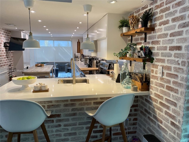 bar featuring sink, a breakfast bar, hanging light fixtures, brick wall, and kitchen peninsula