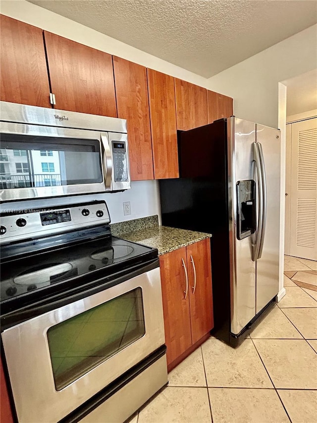 kitchen with stainless steel appliances, light tile patterned floors, a textured ceiling, and dark stone counters