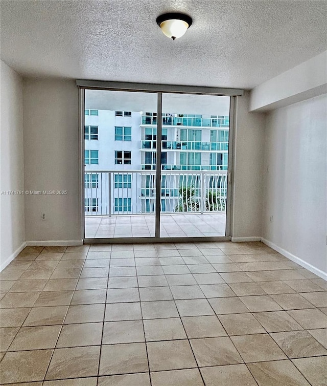 empty room featuring light tile patterned flooring, a wall of windows, and a textured ceiling