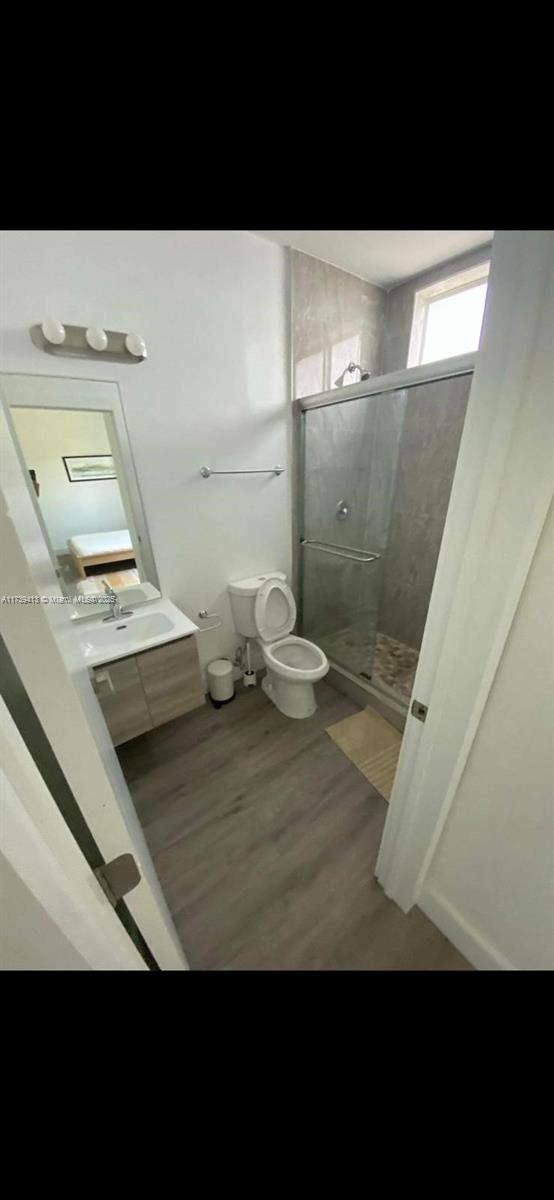 bathroom with vanity, hardwood / wood-style flooring, a shower with shower door, and toilet