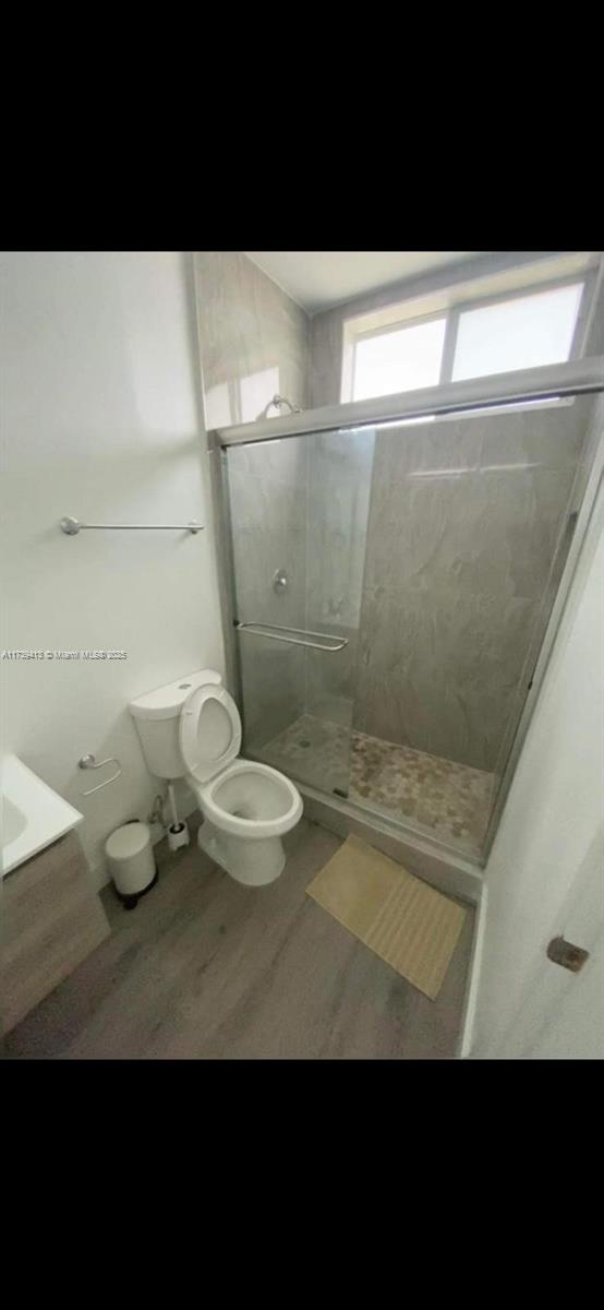 bathroom with wood-type flooring, toilet, a shower with door, and vanity