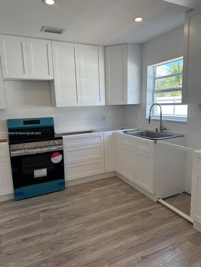 kitchen with white cabinetry, stainless steel electric stove, sink, and light hardwood / wood-style flooring