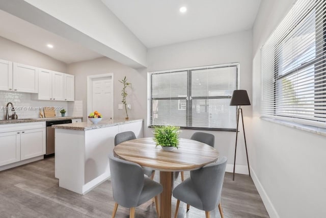 dining space featuring sink, light stone counters, white cabinets, a kitchen island, and light wood-type flooring