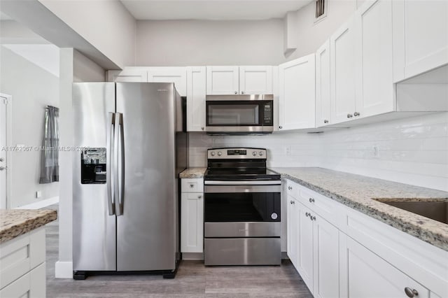 kitchen with dark wood-type flooring, appliances with stainless steel finishes, white cabinetry, light stone countertops, and decorative backsplash