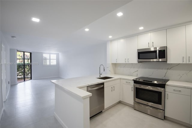 kitchen with appliances with stainless steel finishes, white cabinetry, sink, backsplash, and kitchen peninsula