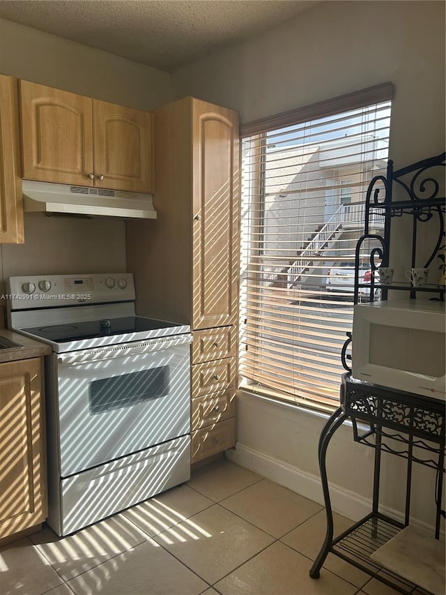 kitchen featuring white electric stove, light tile patterned floors, light brown cabinetry, and a textured ceiling