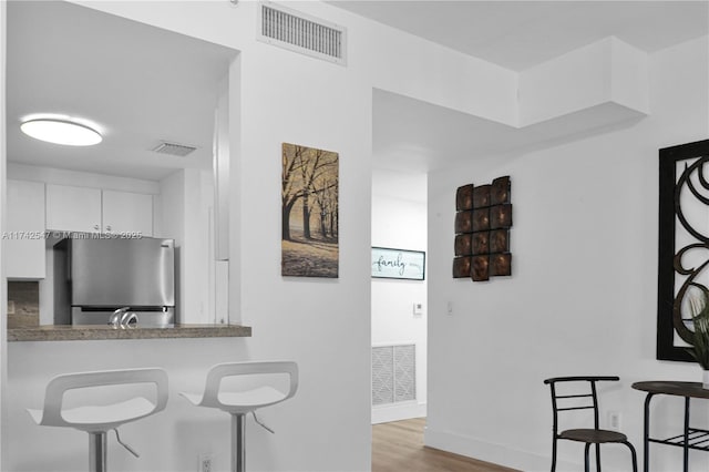 kitchen featuring sink, stainless steel fridge, white cabinetry, kitchen peninsula, and light wood-type flooring