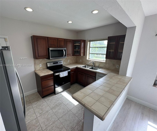 kitchen with tasteful backsplash, sink, tile counters, kitchen peninsula, and stainless steel appliances