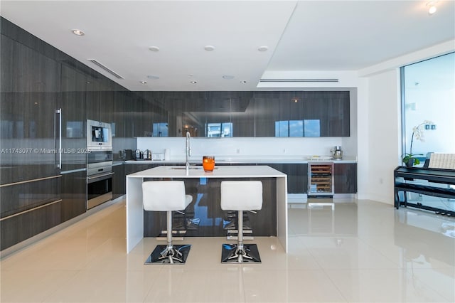 kitchen featuring light tile patterned floors, a kitchen island with sink, a kitchen breakfast bar, wine cooler, and oven