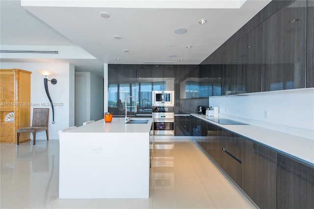 kitchen featuring light tile patterned flooring, sink, stainless steel double oven, black electric stovetop, and a kitchen island with sink