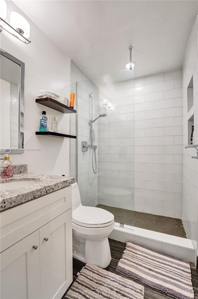 bathroom featuring vanity, wood-type flooring, a tile shower, and toilet