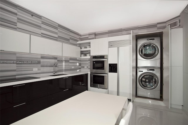 kitchen featuring white cabinetry, sink, paneled built in refrigerator, stacked washer and clothes dryer, and stainless steel double oven