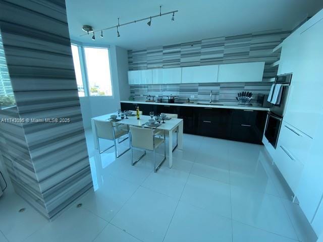 kitchen featuring sink, light tile patterned floors, backsplash, a center island, and white cabinets