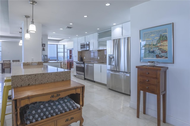 kitchen featuring appliances with stainless steel finishes, light stone countertops, decorative light fixtures, decorative backsplash, and white cabinetry