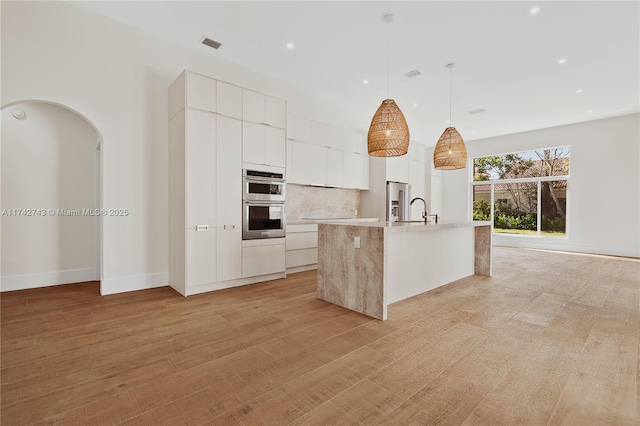 kitchen featuring pendant lighting, white cabinets, a kitchen island with sink, stainless steel appliances, and light hardwood / wood-style flooring