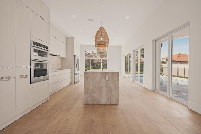 kitchen with pendant lighting, sink, stainless steel appliances, white cabinets, and light wood-type flooring