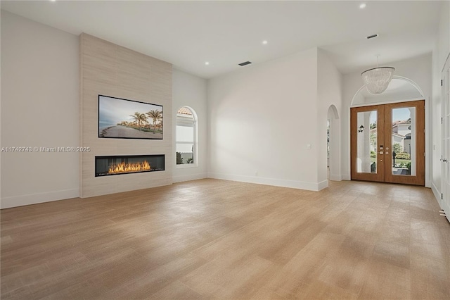 unfurnished living room featuring a large fireplace, light hardwood / wood-style flooring, and french doors