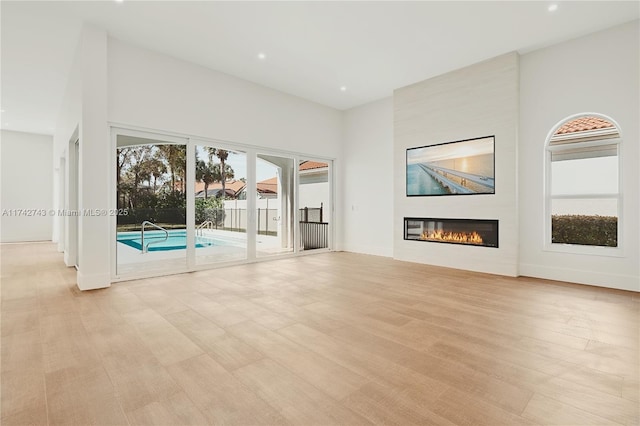 unfurnished living room with a fireplace, light hardwood / wood-style floors, and a high ceiling