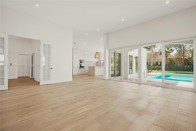 unfurnished living room featuring french doors, a towering ceiling, and light hardwood / wood-style floors