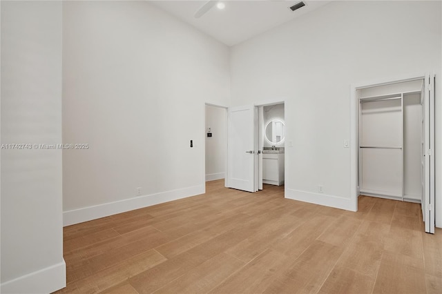 unfurnished bedroom featuring a walk in closet, a towering ceiling, sink, and light hardwood / wood-style flooring