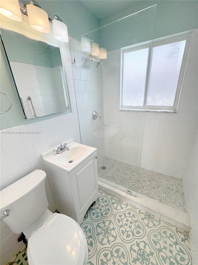 bathroom with tiled shower, tile patterned floors, toilet, tile walls, and vanity