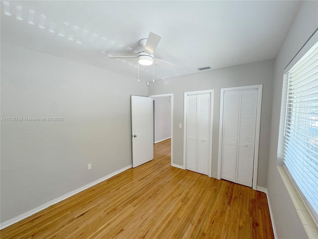 unfurnished bedroom featuring ceiling fan, light wood-type flooring, and two closets