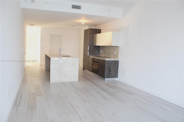 kitchen with dark brown cabinetry, sink, tasteful backsplash, light hardwood / wood-style flooring, and black electric cooktop