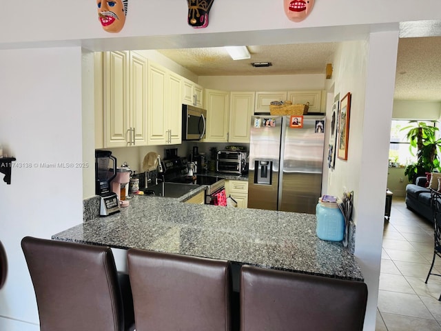 kitchen with cream cabinetry, stainless steel appliances, light tile patterned flooring, a textured ceiling, and a peninsula