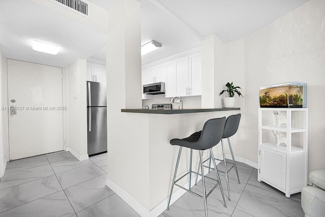 kitchen with white cabinetry, a breakfast bar, kitchen peninsula, and appliances with stainless steel finishes