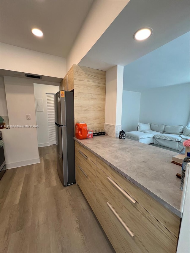 kitchen featuring backsplash, light hardwood / wood-style flooring, stainless steel refrigerator, and light brown cabinets