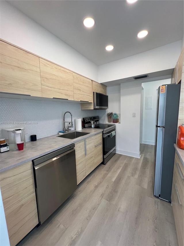 kitchen featuring appliances with stainless steel finishes, sink, decorative backsplash, light brown cabinets, and light hardwood / wood-style flooring