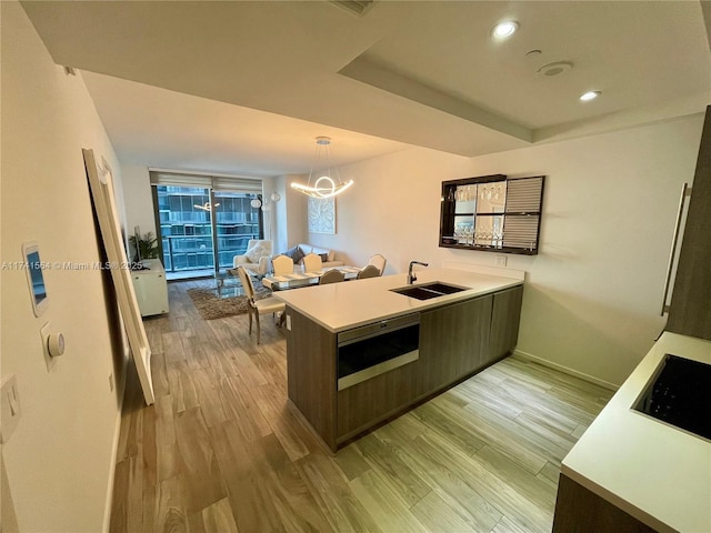 kitchen with dark brown cabinetry, sink, a chandelier, kitchen peninsula, and light hardwood / wood-style floors