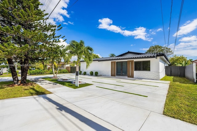 view of front of home featuring a front yard, a tile roof, fence, and stucco siding