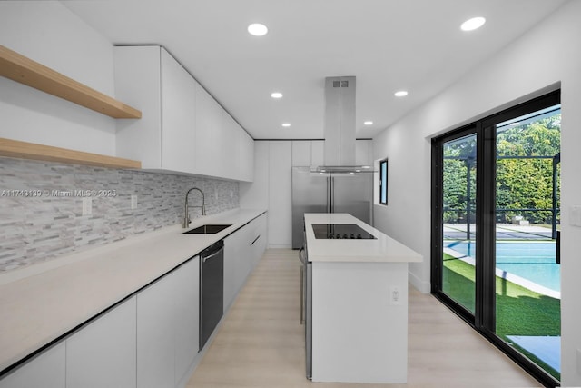 kitchen with island exhaust hood, open shelves, light countertops, white cabinetry, and a sink