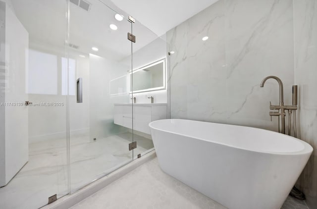 bathroom with marble finish floor, a marble finish shower, visible vents, a freestanding bath, and stone wall