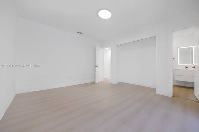 unfurnished bedroom featuring baseboards, visible vents, connected bathroom, light wood-type flooring, and a closet