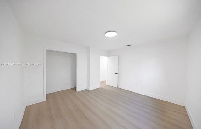 unfurnished bedroom featuring light wood-type flooring, baseboards, visible vents, and a closet