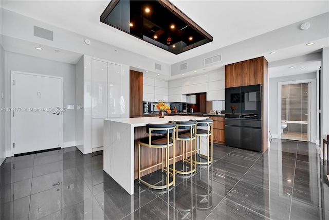 kitchen featuring white cabinetry, a kitchen island, a breakfast bar area, and black fridge