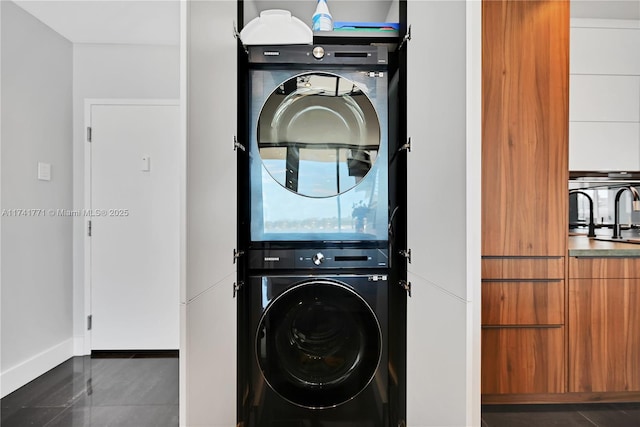 laundry room featuring stacked washer / drying machine and dark tile patterned flooring