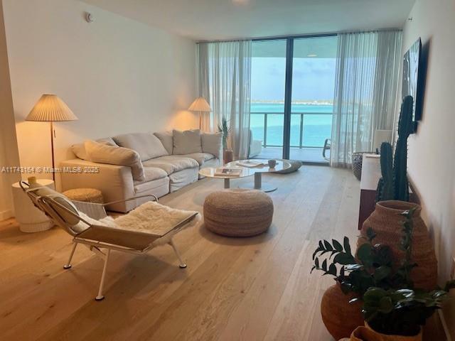 sitting room featuring floor to ceiling windows, a water view, and light wood-type flooring