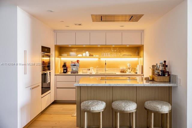 bar featuring sink, light hardwood / wood-style floors, black double oven, and white cabinets