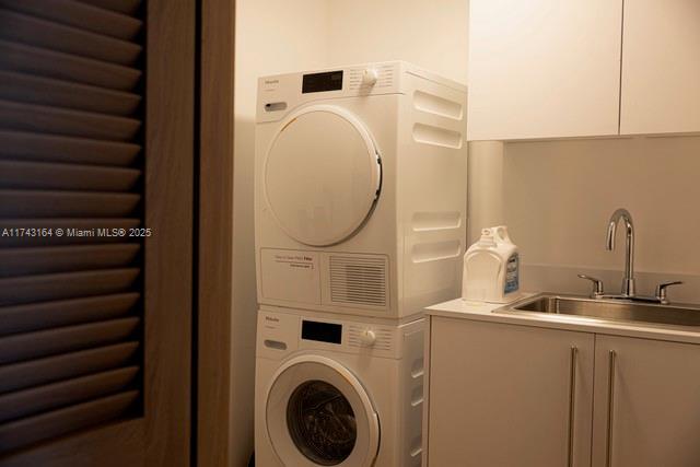 clothes washing area with stacked washer / drying machine, cabinets, and sink