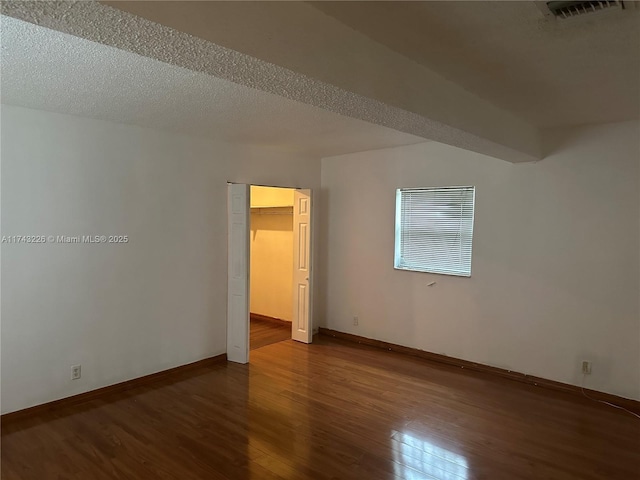 empty room with dark wood-style floors, baseboards, visible vents, and a textured ceiling