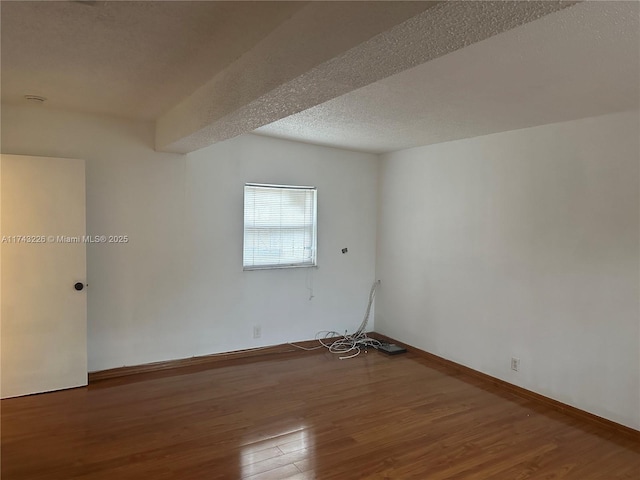 empty room with a textured ceiling, baseboards, and wood finished floors