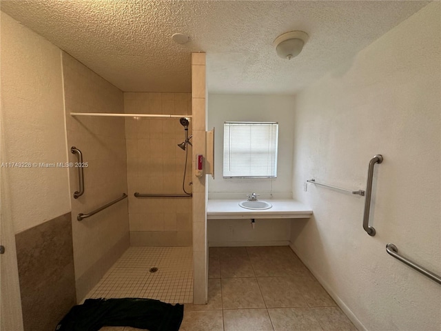 bathroom with a textured ceiling, a textured wall, tile patterned flooring, and a tile shower