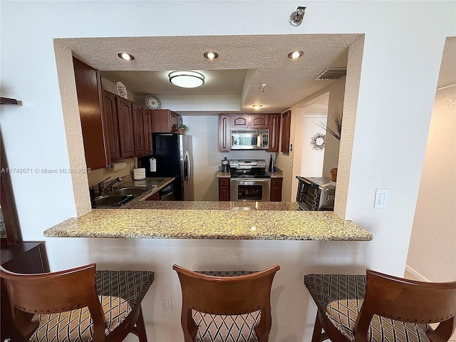 kitchen featuring stainless steel appliances, sink, a textured ceiling, and kitchen peninsula