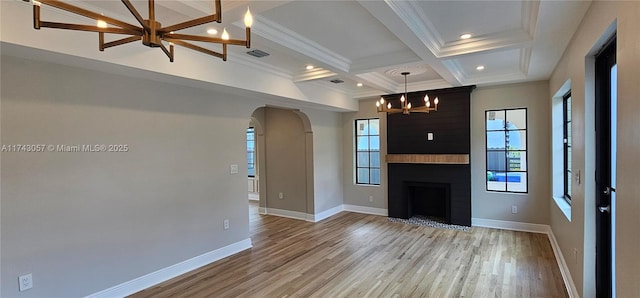 unfurnished living room featuring baseboards, visible vents, light wood finished floors, arched walkways, and a chandelier