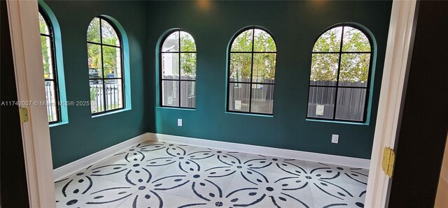 tiled empty room featuring plenty of natural light and baseboards