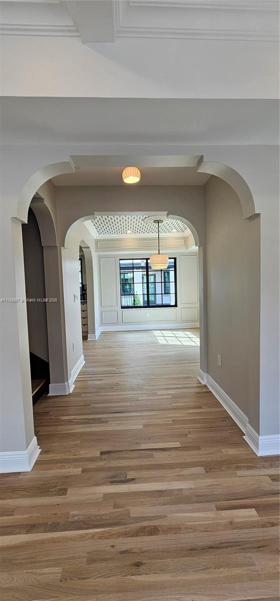 hall with baseboards, arched walkways, and wood finished floors